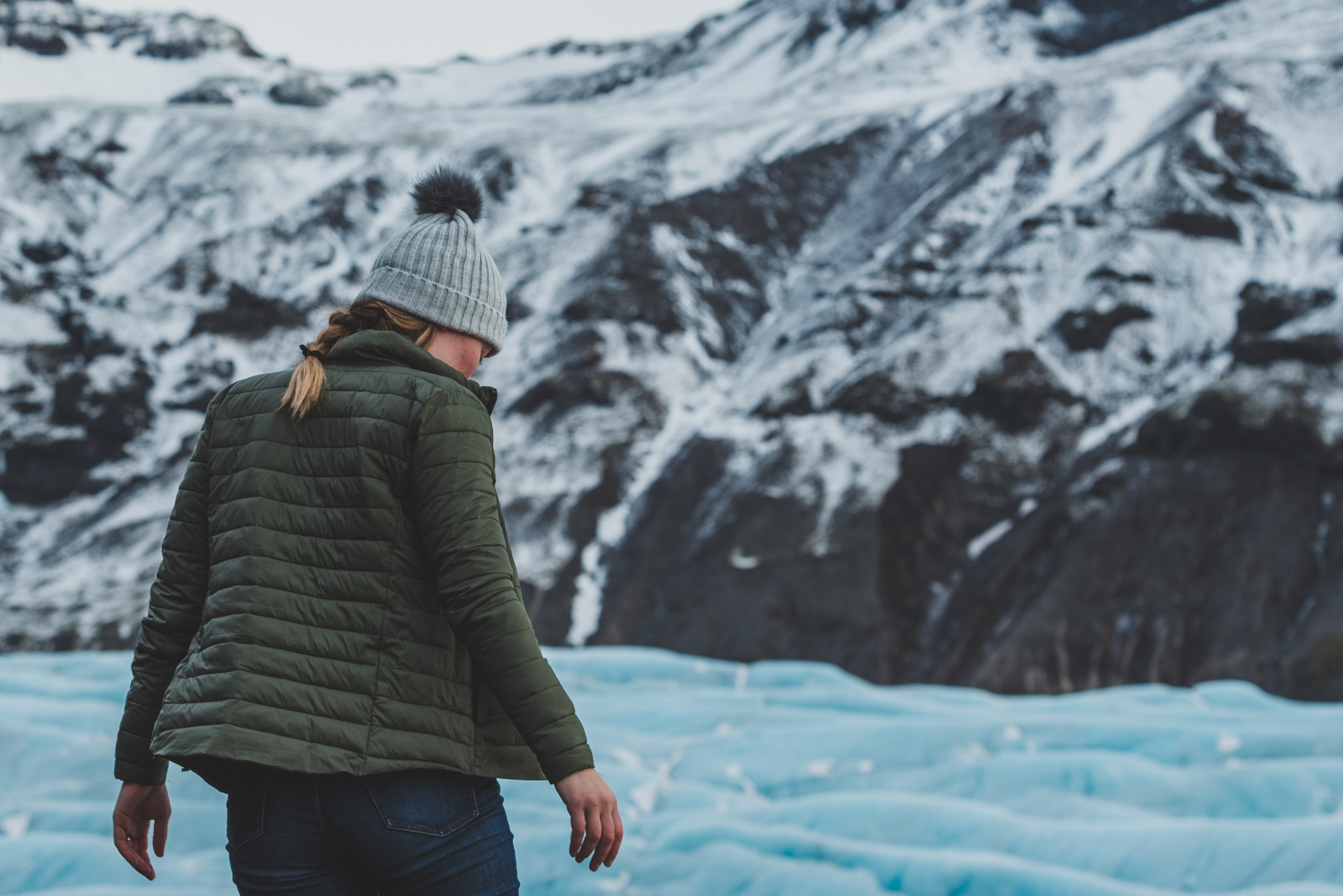 Female observing glacier in puffy green jacket and knit cap