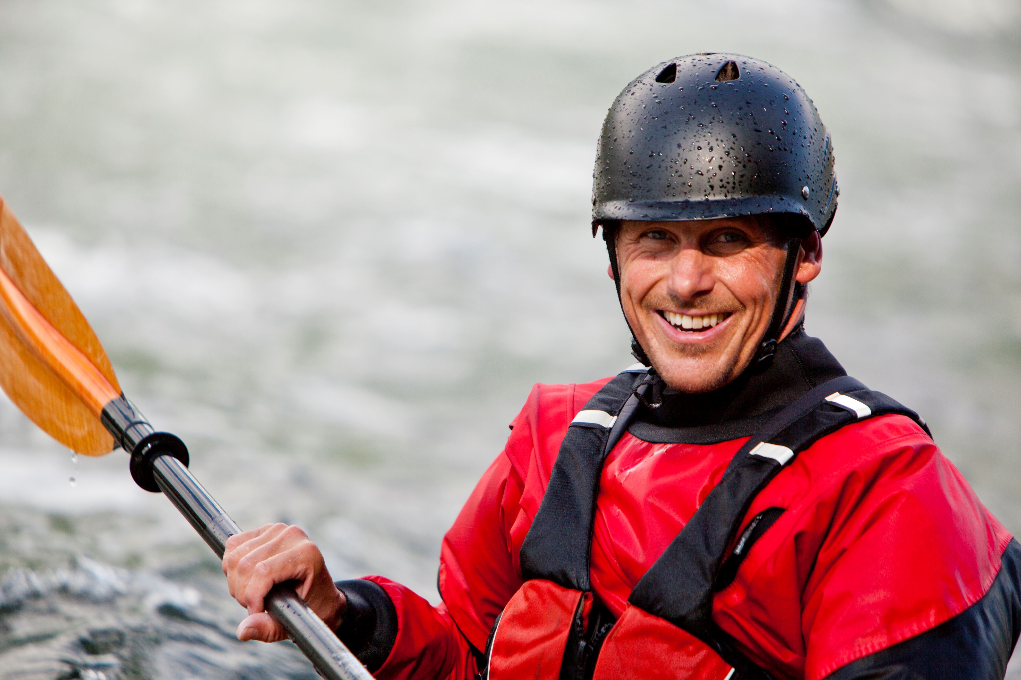 Professional kayaker smiles for a quick photo while paddling in full white water gear